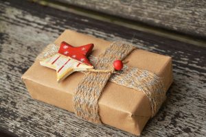 A small box, wrapped in brown paper with a twine ribbon and red and white star ornament sits on a woven placemat.